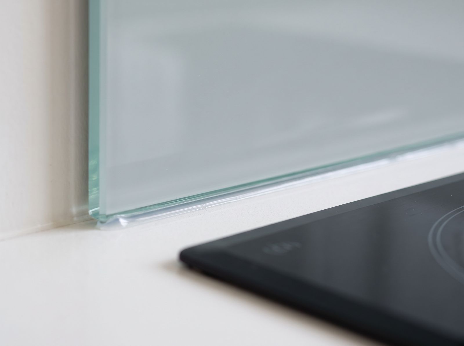 Close-up of a glass splashback edge meeting a dark benchtop