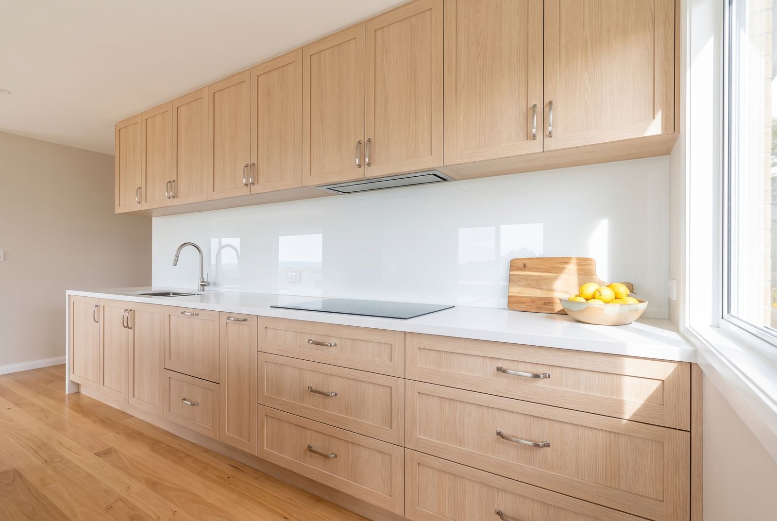 Pale timber kitchen with a white glass splashback