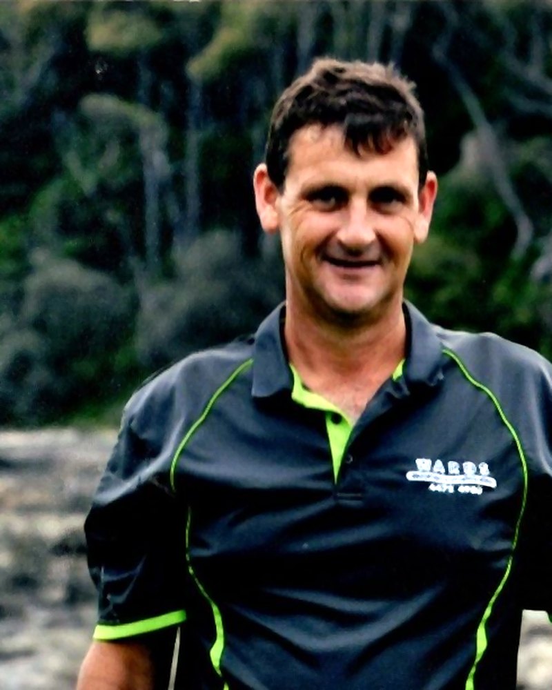Ryan 'Wardy' Ward of Wards Wardrobes & Showerscreens, smiling outdoors in his charcoal and lime Wards work polo